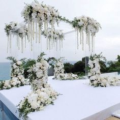 an outdoor wedding setup with white flowers and greenery on the table, overlooking the ocean