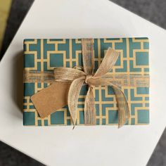 a wrapped gift box with a brown ribbon and tag on it sitting on top of a white table