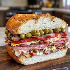 a close up of a sandwich on a wooden board with olives and meat in it