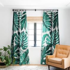 a living room with a chair, plant and window curtain in it's corner