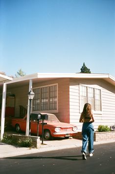 a woman standing in front of a house next to a red car