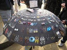 an umbrella is covered with earrings and earring hooks as people walk by in the background