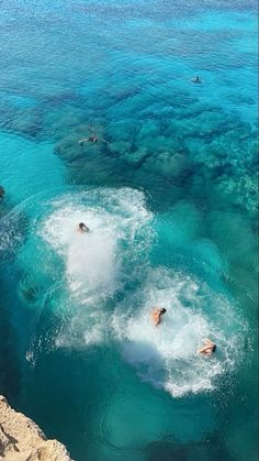 several people swimming in the water near some rocks