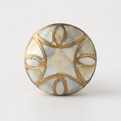 a white and gold button with an intricate design on the front, sitting on a white surface