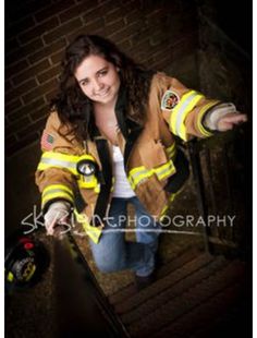 a woman dressed in fire fighter gear standing on stairs with her arms out and pointing at the camera