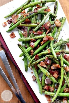 cooked green beans with bacon on a white platter next to silver utensils