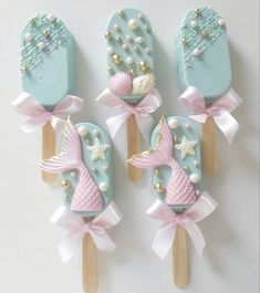 four ice cream pops decorated with pink and blue icing, seashells and pearls