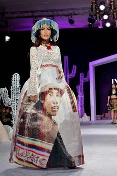 a woman is walking down the runway in a long dress with a large hat on her head