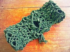 a green crocheted scarf laying on top of a wooden table