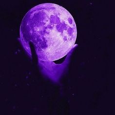 a person's hand holding the moon in front of them with purple hues