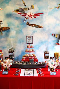 a red table topped with lots of cakes and desserts next to an airplane painted on the wall