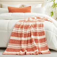 an orange and white blanket sitting on top of a bed next to a potted plant