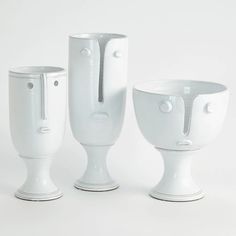 three white vases sitting next to each other on top of a table in front of a white background