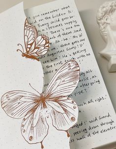 an open book with a butterfly on it next to a wax stamp and a statue