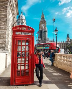 a woman standing next to a red phone booth