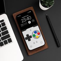 an iphone case with a game controller on it next to a laptop computer and pen