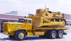 a large yellow truck is parked in front of a building with a crane on the back