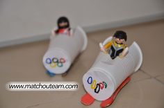 two toy figurines sitting on top of a white object with olympic symbols painted on it