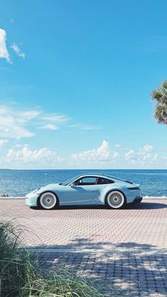 a blue sports car parked in front of the ocean on a sunny day with palm trees