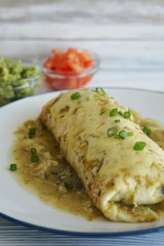 an enchilada on a white plate with green onions and tomatoes in the background