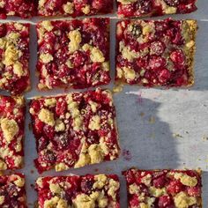 several squares of cranberry bars are arranged on a sheet of paper with crumbs