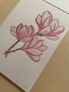 a drawing of two pink flowers on a white paper with wood table in the background