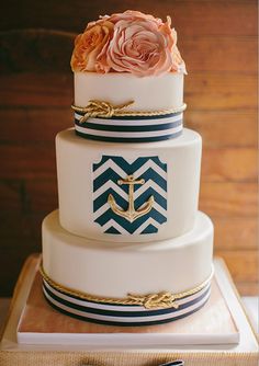 a three tiered wedding cake with an anchor and rose on the top, sitting on a wooden table