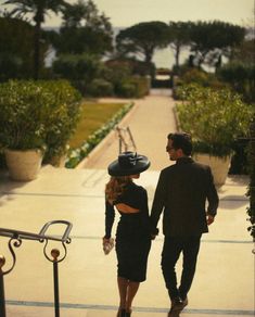 a man and woman walking down a sidewalk holding hands while wearing black outfits with hats on their heads