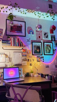 a laptop computer sitting on top of a wooden desk next to a wall covered in pictures