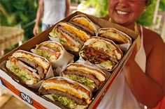 a woman holding up a box full of sandwiches