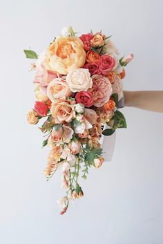 a bridal bouquet is being held up by someone's hand in front of a white wall