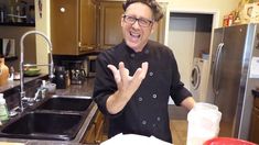 a man standing in front of a kitchen sink making the peace sign with his hands