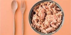 a metal bowl filled with meat next to a fork and knife on an orange surface