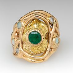 This awesome 14K yellow gold organic, freeform style ring is centered with an 18K yellow gold nugget with a bezel set, round mixed cut emerald, weighing 0.71 carats, in the middle. The shoulders are accented with a total of three (3) round, opal cabochons and two (2) round brilliant cut diamonds in bezel settings. The ring measures 23.8mm at the top, rises 4.7mm above the finger, tapering to 5.5mm wide and 22.1mm thick at the base of the shank. This ring is currently a size 7.5. The emerald shows abrasion and a light scratch/surface reaching natural inclusion. Unique Gold Emerald Ring Birthstone, Unique Gold Emerald Ring With Bezel Setting, Unique Yellow Gold Emerald Ring With Bezel Setting, Unique Emerald Ring In 14k Gold, Gold Nugget, Round Brilliant Cut Diamond, Bezel Setting, Round Brilliant, Emerald