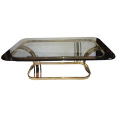 a glass and brass coffee table with two metal bars on the bottom, against a white background