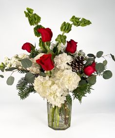 a vase filled with flowers and greenery on top of a white table next to a pine cone