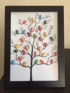 a tree with birds painted on it in a black frame, sitting on a table