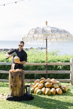 a man standing next to a pile of coconuts under an umbrella in the grass