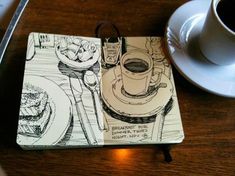 an open notebook sitting on top of a wooden table next to a cup of coffee