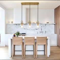 a kitchen with marble counter tops and white cabinets, along with three beige bar stools