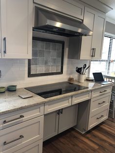 a kitchen with white cabinets and marble counter tops, an open laptop on the stove