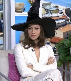 a woman wearing a witches hat sitting on top of a white couch next to a potted plant