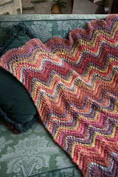 a crocheted blanket sitting on top of a green couch next to a pillow