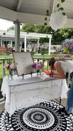 a woman writing on a table with flowers in vases next to it and an umbrella