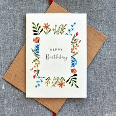 a card with the words happy birthday written in floral designs on it, sitting on top of a brown envelope