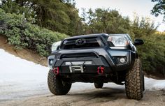 a black toyota truck driving down a snow covered mountain side road with trees in the background