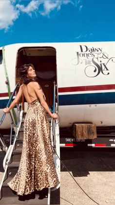 a woman in a leopard print dress stepping out of an airplane with luggage on the steps