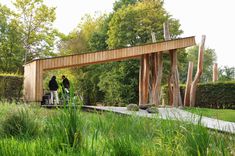 two people standing under a wooden structure in the grass