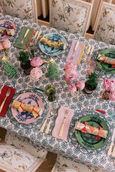 the table is set with plates, silverware, and pink flowers on blue floral napkins