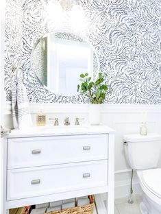 a white toilet sitting next to a bathroom sink under a mirror and a plant in a vase